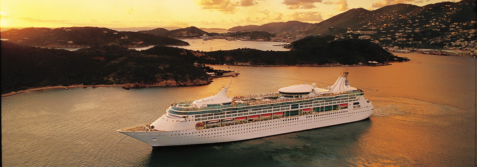 Bild på Rhapsody of the Seas, taget från sidan, utanför en Karibisk ö i solnedgången.