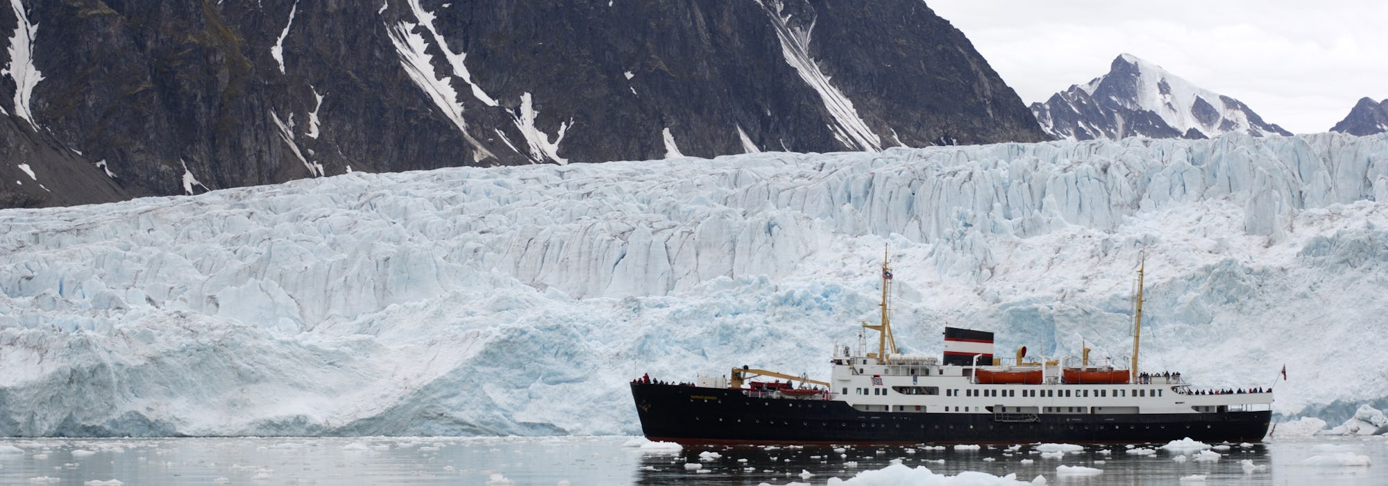 Fartyget MS Nordstjernen kryssar sig fram i islandskapet på Svalbard med isberg och snötäckta berg i bakgrunden.