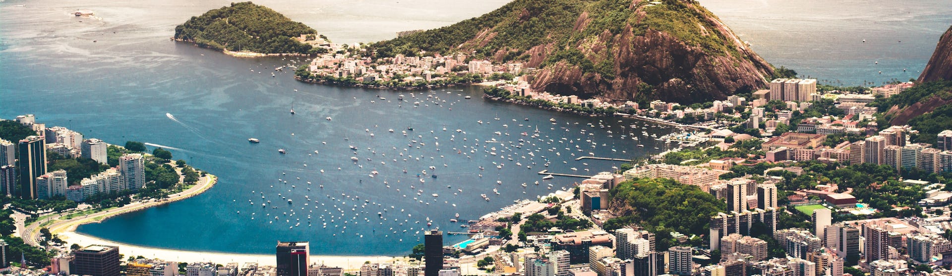 Foto på Rio de Janeiro från ovan med byggnader, berg och kristallblått vatten.