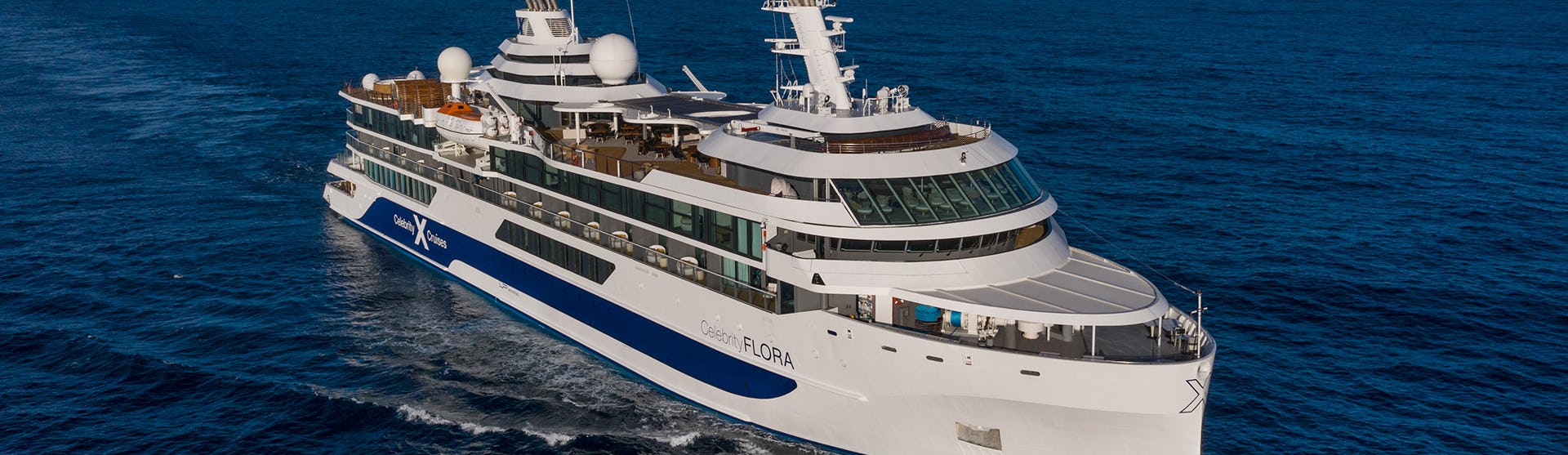 Det mindre fartyget Celebrity Flora kryssar sig fram i klartblått vatten.