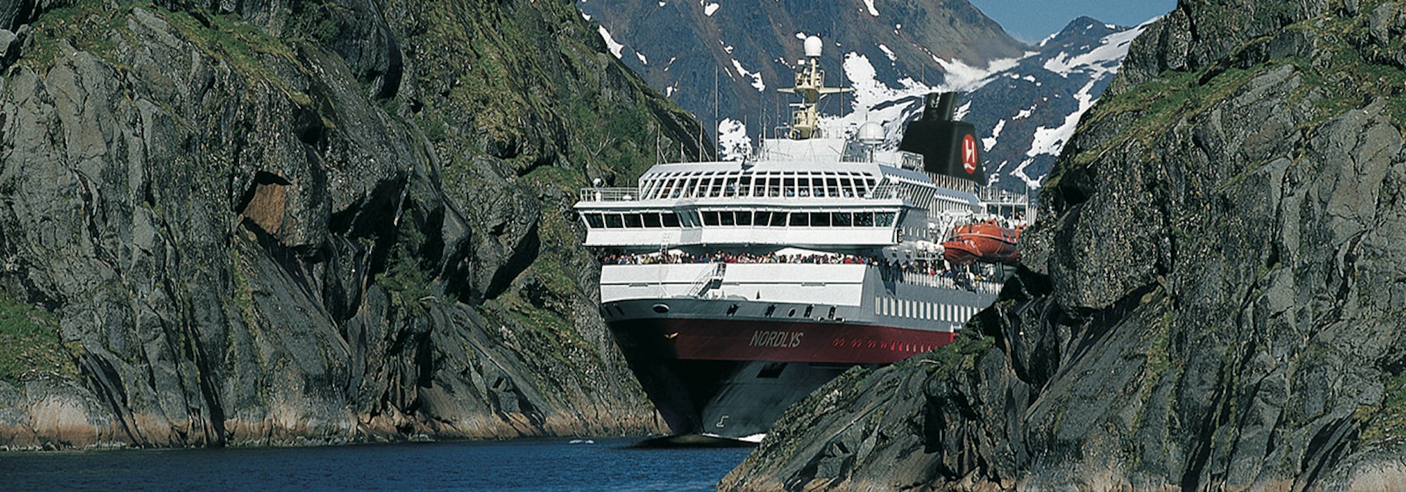 Fören på MS Nordlys sticker fram mellan bergen i de norska fjordarna.