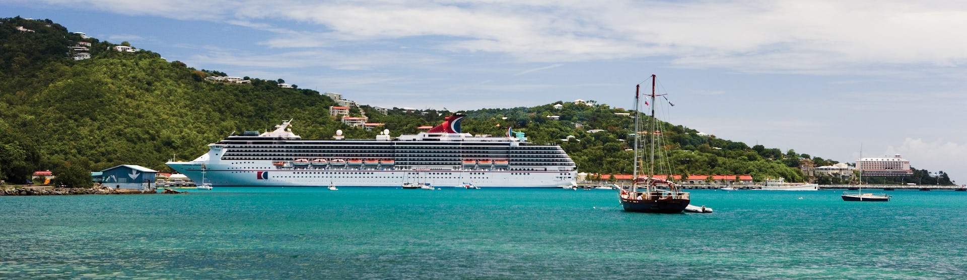 Carnival Legend ligger ankrad i en vacker hamn med klart blått vatten med gröna berg i bakgrunden.