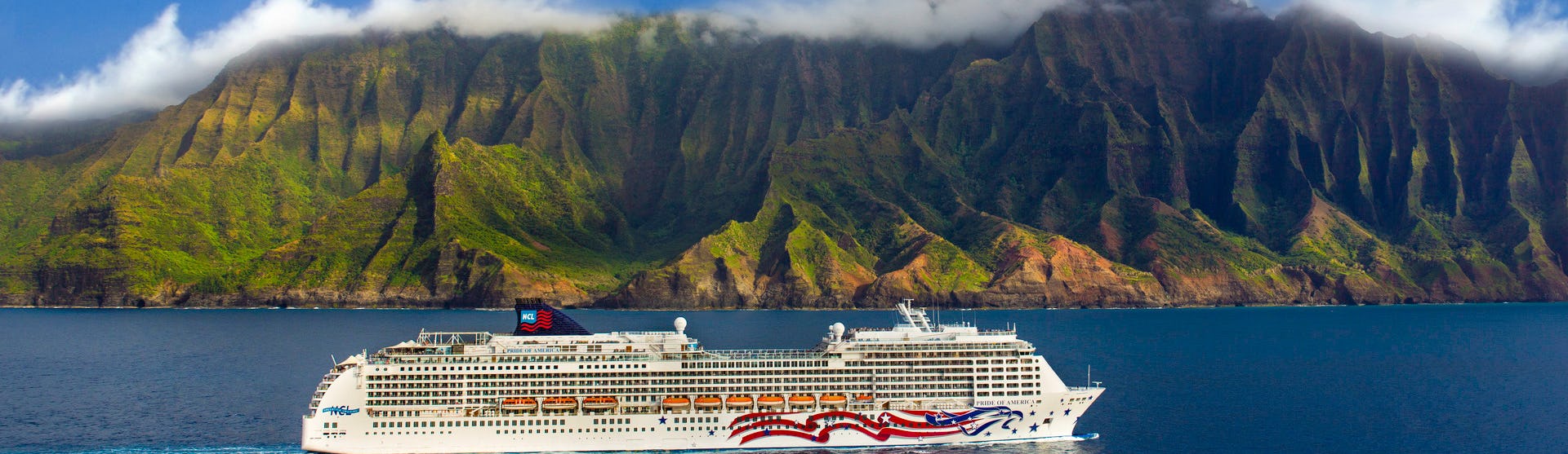 Fartyget Pride of America kryssas i det kristallblå vattnet utanför Hawaiis kust med storslagen natur och berg i bakgrunden.