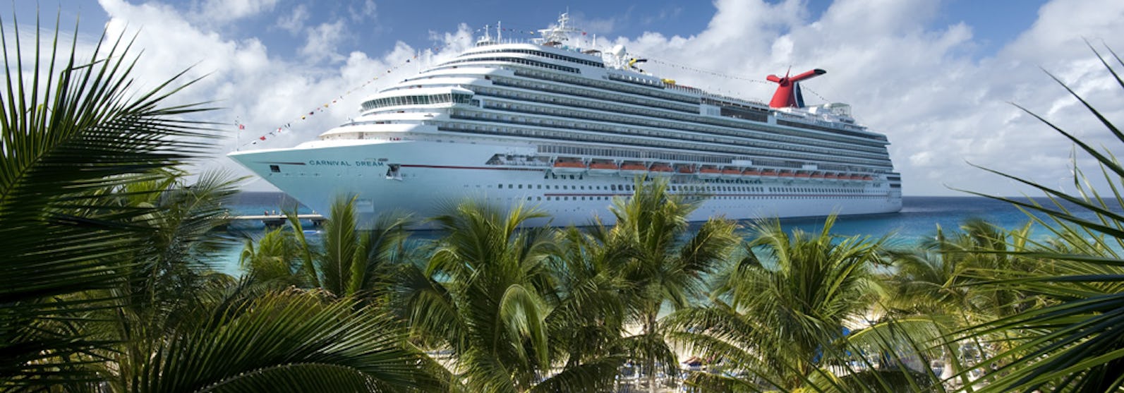 Bild på fartyget Carnival Dream. I förgrunden syns en sandstrand med solsängar och flera gröna palmer.