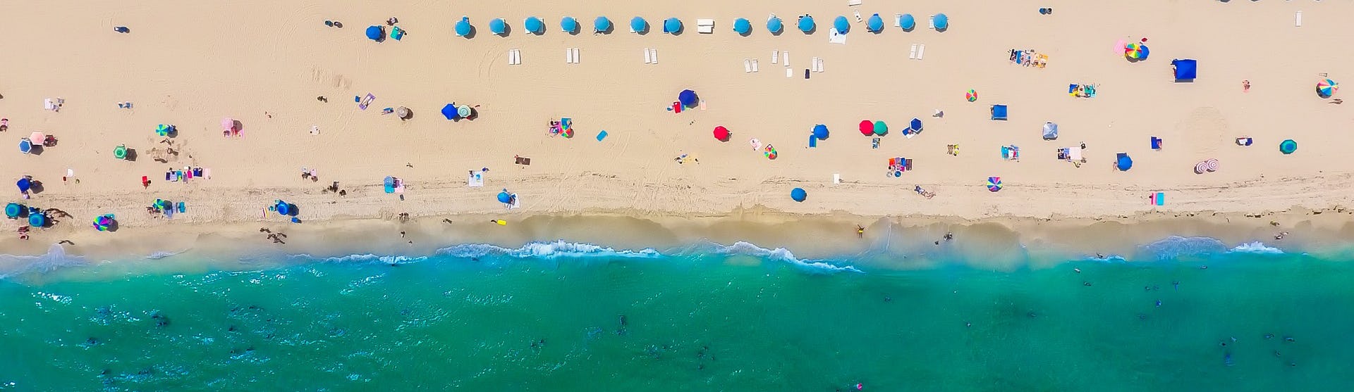 Bild från ovan på en strand i Fort Lauderdale med vatten i nederkant och massor av parasoll. 