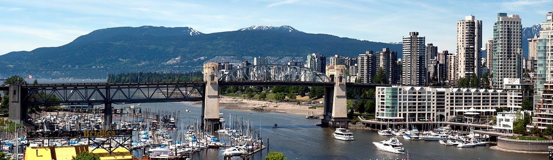 En mindre hamn i Vancouver med stadens skyskrapor till höger i bild och bergen som tornar upp sig.
