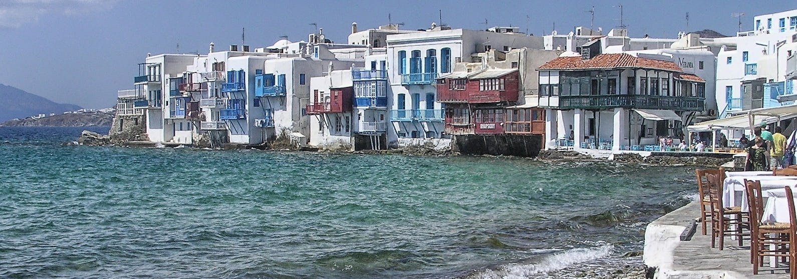 Vågorna slår in mot stranden med färgglada hus runtomkring i Mykonos, Grekland.