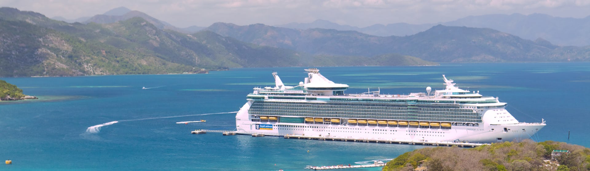 Fartyget Freedom of the Seas ligger vid en hamn i Karibien med ljusblått vatten och höga berg i bakgrunden.