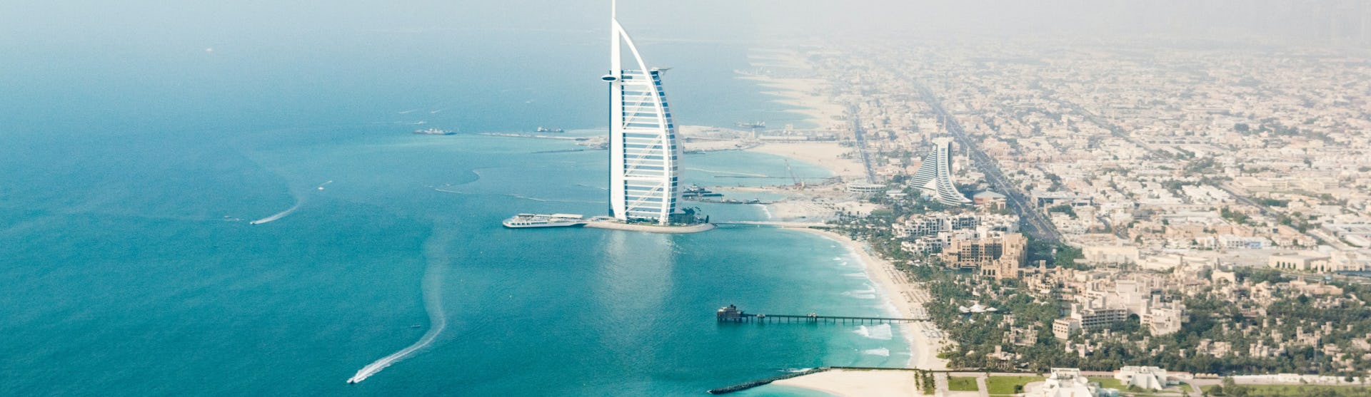 Överblicks bild över Dubais hamn med byggnader stränder och klarblått vatten.