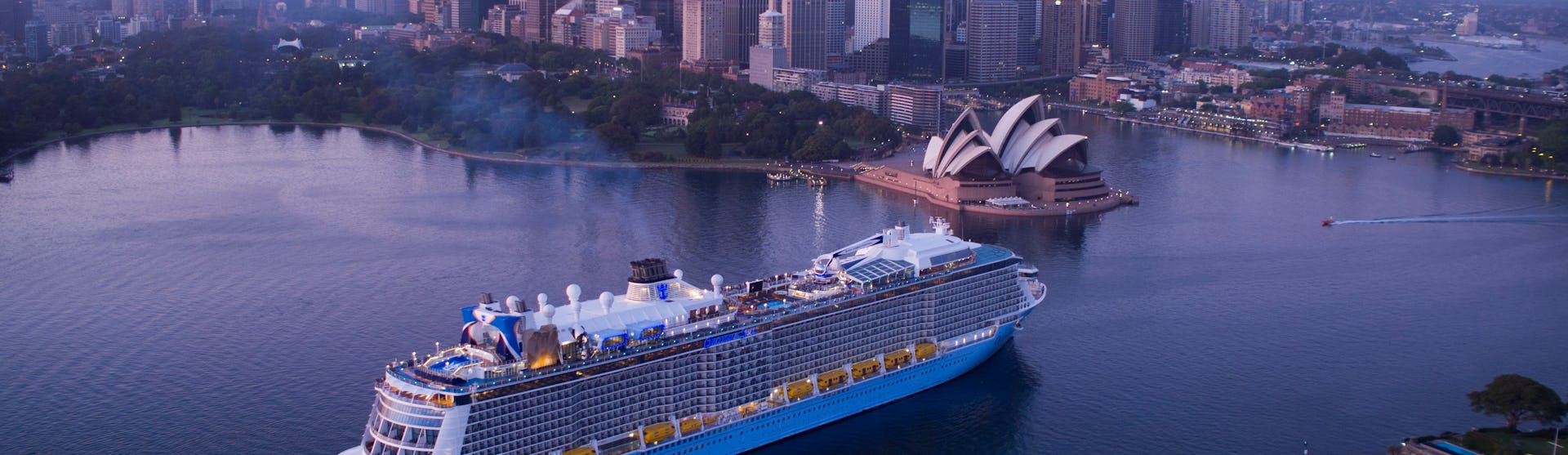 Ovation of the Seas kryssar förbi Sydneys ikoniska operahus med stadens skyskrapor som uppenbarar sig bakom.