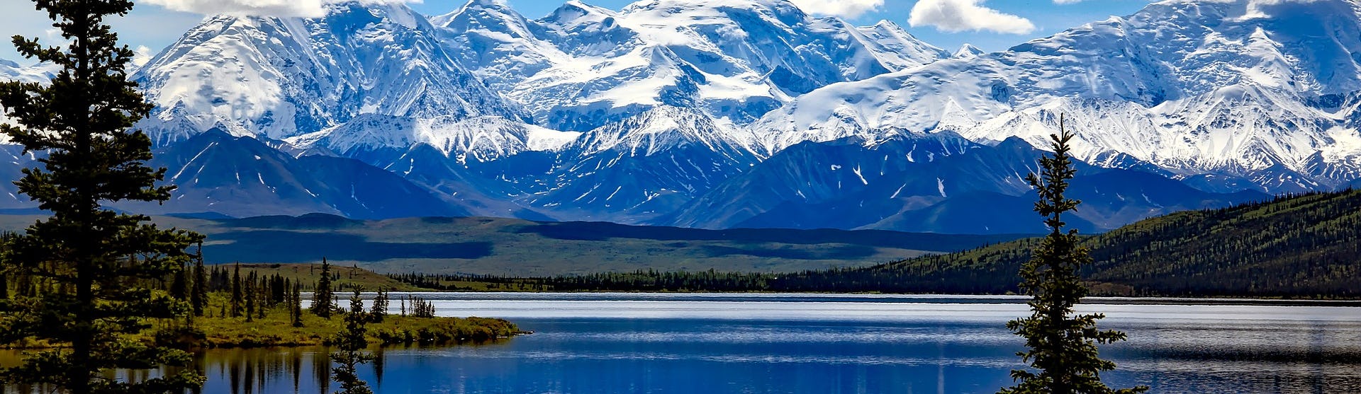 Alaskas oslagbara natur med skog, snötäckta berg och stilla vatten.
