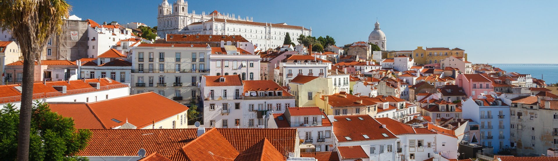 Bild från ovan på färgglada hus i Lissabon med havet i bakgrunden. 