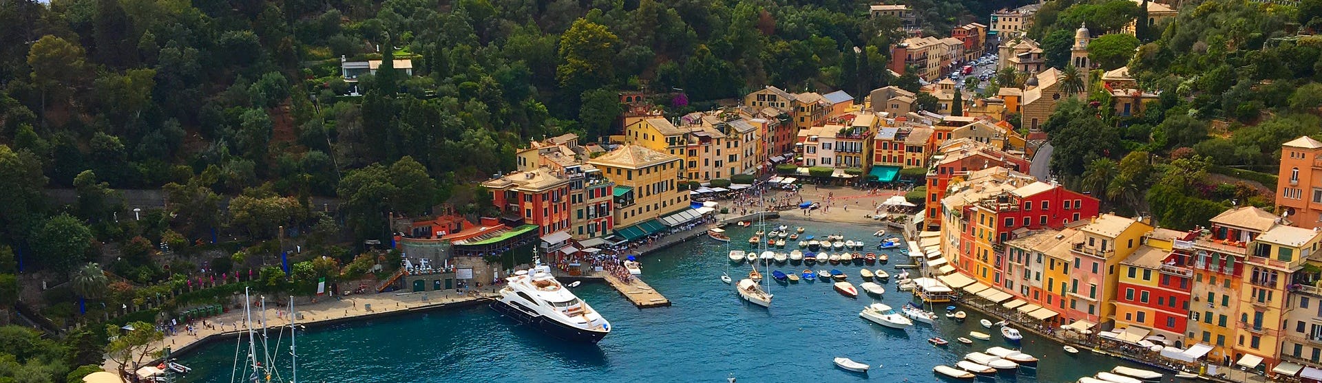 Portofinos hamn med båtar, gröna träd och färgglada hus.